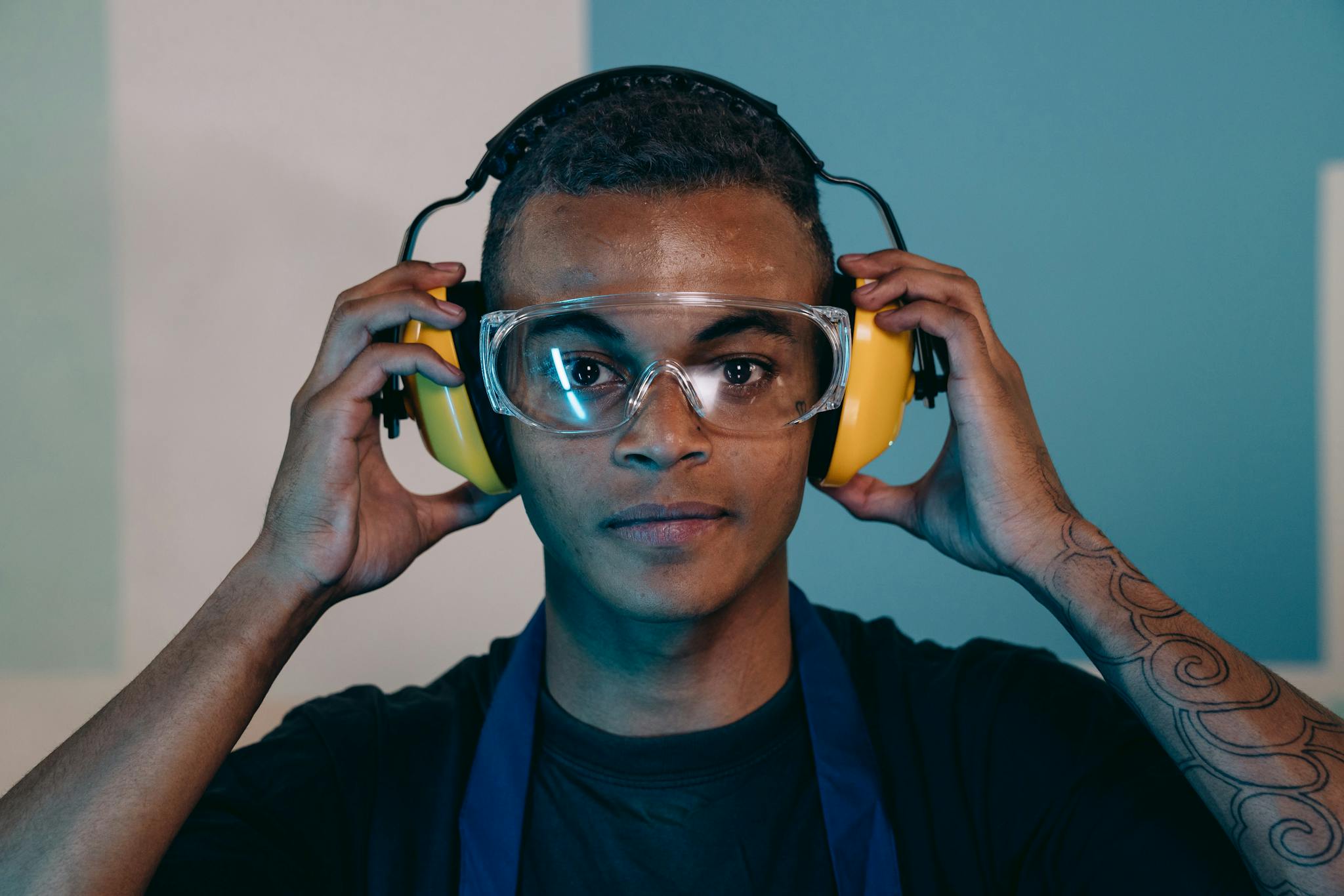 Close-up portrait of a young male engineer wearing safety glasses and earmuffs in an industrial setting.